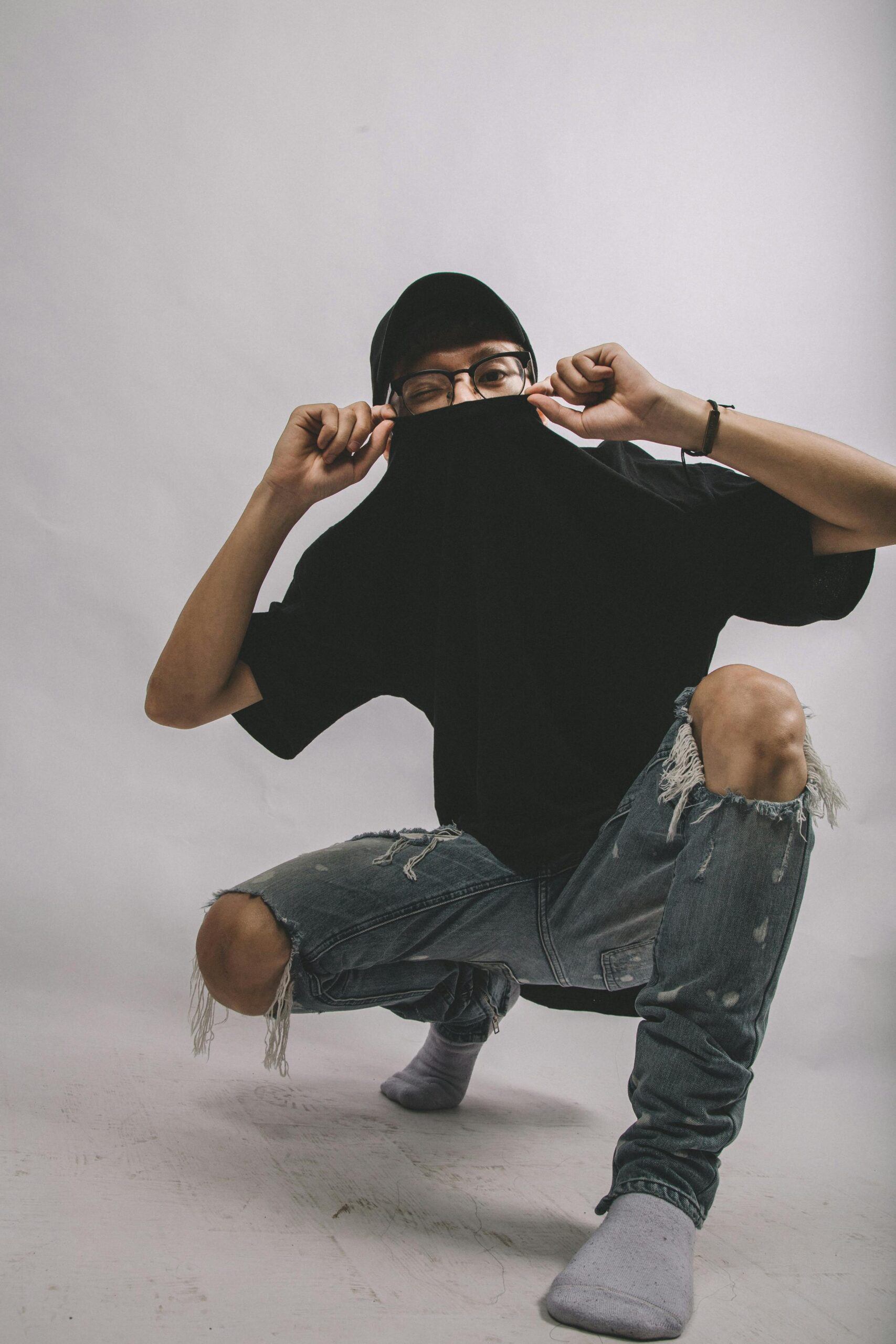 Stylish young adult posing with ripped jeans and cap in a studio setting.